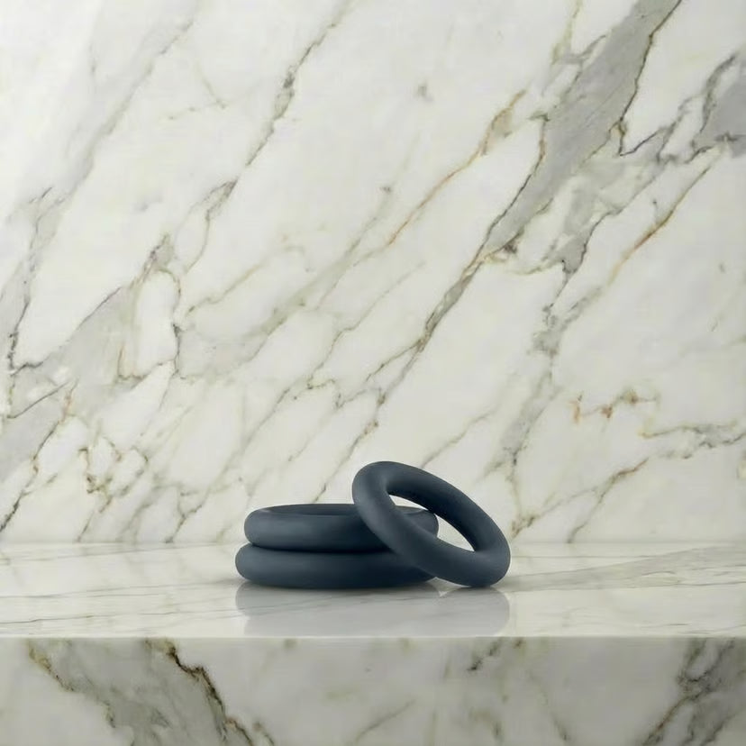 Drie donkergrijze siliconen cockringen in verschillende maten op marmeren plank